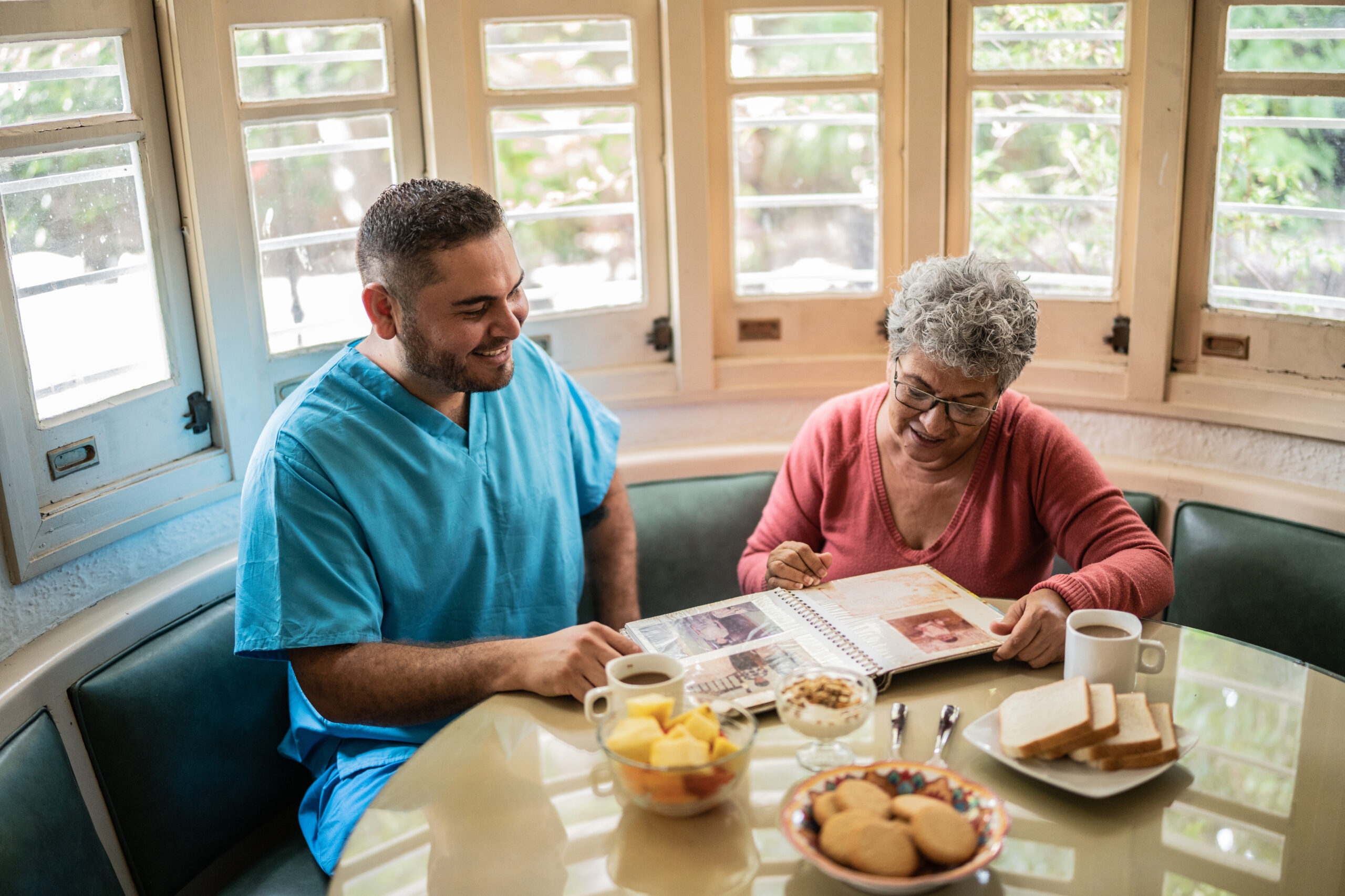 Senior woman and mid adult nurse looking at photo album in the dining room in a nursing home